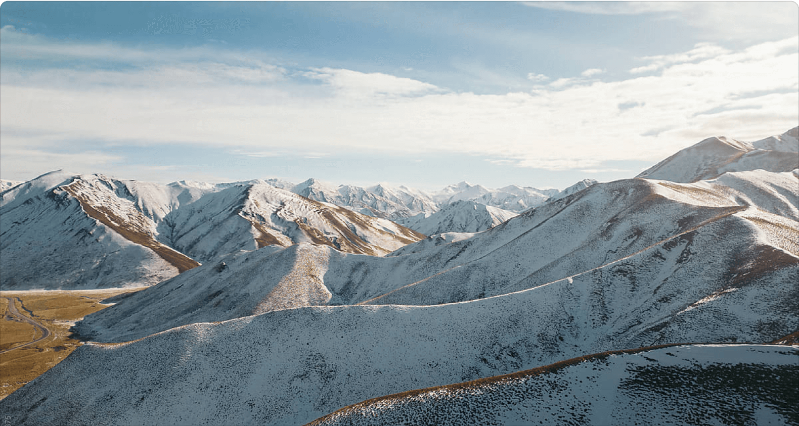 Stunning panoramic view of snow-capped mountains under a clear blue sky, showcasing the rugged terrain and rolling hills of a high-altitude landscape. Ideal for nature lovers and adventure enthusiasts.