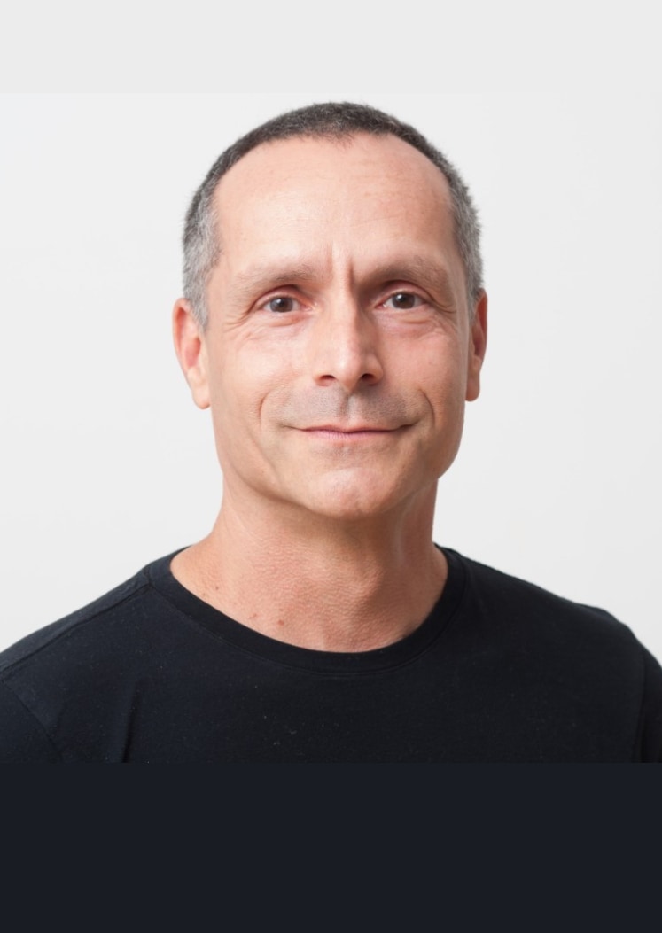 Smiling middle-aged man with short hair wearing a black t-shirt, posing against a light background.